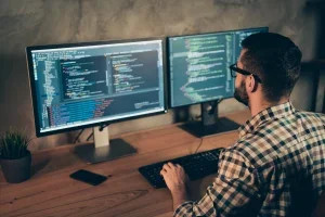 man looking at javascript on two monitors 